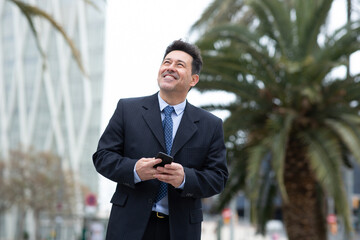 Happy mature businessman walking in the city with cellphone