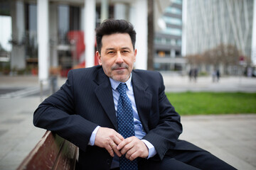 Mature latin businessman sitting on bench outside in the city