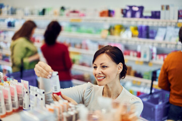 A pretty female customer with a bun hair picks hand cream from the shelf.