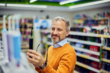A grey-bearded senior male customer holding an electric toothbrush in a store.