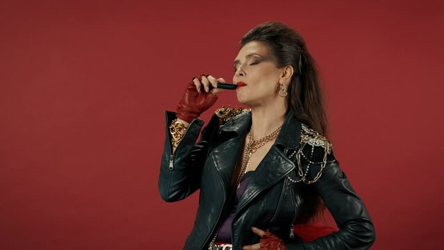 A woman takes a puff on an electronic cigarette and starts coughing. Profile portrait of a woman with bright makeup, in a leather jacket with chains on an isolated red background. Advertising.