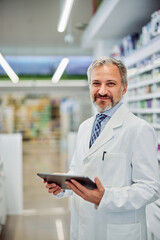 Naklejka na ściany i meble Portrait of a smiling male pharmacist holding a digital tablet in a workplace.