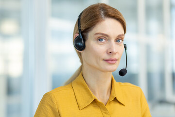 Portrait of a young woman in a headset sitting in the office and looking seriously at the camera. Employee of the hotline, support service. Close-up photo.