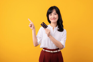 Portrait beautiful young asian woman enterpriser happy smile wearing white shirt and red plants pointing finger gesture to free copy space and holding credit card isolation on yellow background.