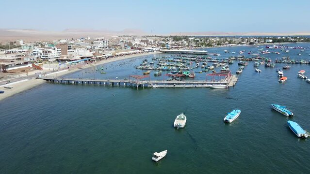 Aerial shot drone flies forward over boat marina with wooden pier in Paracas, Peru