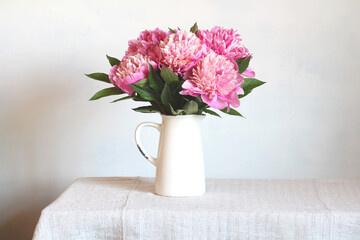 a lush bouquet of pink peonies in a white jug on a table on a white background.