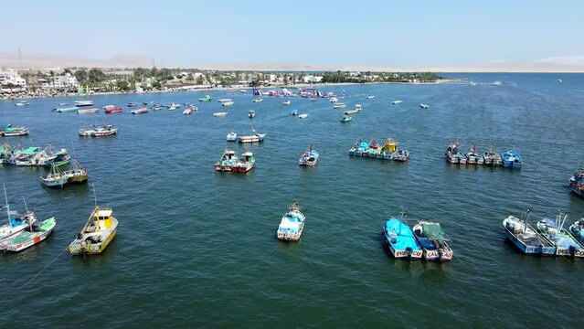 Aerial shot drone flies over boats in Paracas harbor toward aquatic inflatable park