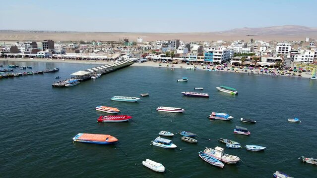 Aerial shot drone flies over boats and pier in Paracas harbor toward desert in the distance