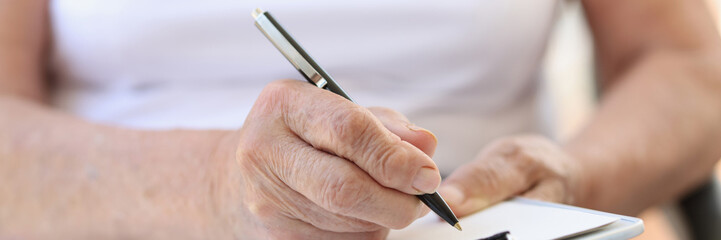 Old woman filling form with pen in clinic or in hospice