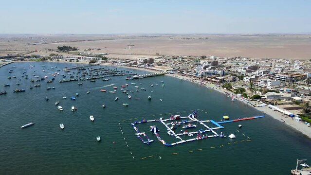 Aerial shot drone flies over inflatable aquatic park toward the desert in Paracas National Reserve