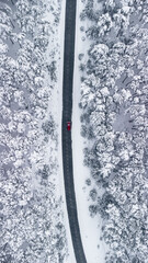 a red car passes through a road in a frozen forest, drone shot