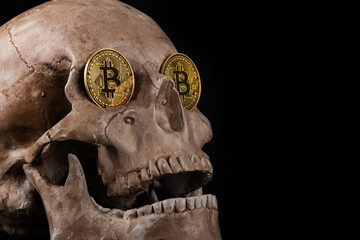 A gold coin with the Bitcoin cryptocurrency symbol in the eye sockets of a human skull 