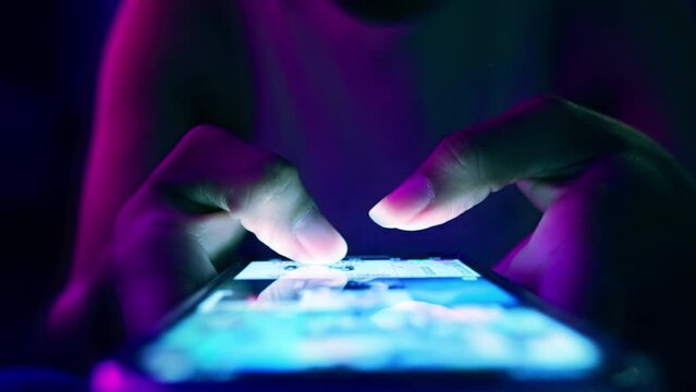 Finger of woman touching scroll page app on mobile phone.In a room with blue and purple neon tones.concept Social media and marketing