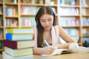 Smiling student girl in eyeglasses reading a red book in a library. School and education concept
