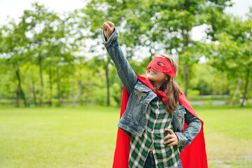 Girl Plays Superhero. Happy girl are playing superhero. Kid run across green field in red cloak at...