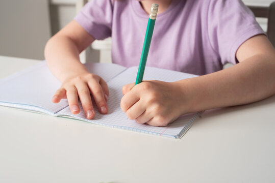 Close-up of children's hands. Left-hander writes in a notebook on the table. International Left Handers Awareness Day