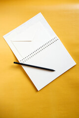 Notebook envelope and black pencil lying on yellow background . Write a letter, postal services, email. Mailing services, writing materials, paper goods