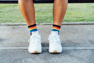 Fototapeta na wymiar Close up LGBT persons legs wearing rainbow socks and white shoes on concrete ground. Loneliness, sadness for homosexual discrimination. Fight for equality, freedom, human rights. Pride month.