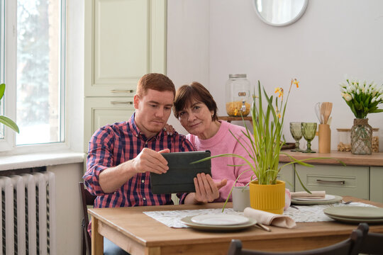 Moments of Connection: A candid shot showing a young man and an older woman engrossed in an interaction through a tablet - Powered by Adobe