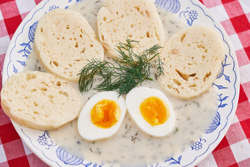 Top view on boiled egg, bread dumplings and fresh dill stalk in the creamy dill sauce on rustic blue onion porcelain plate. Traditional, seasonal dish from cuisine of Czech republic and Slovakia.