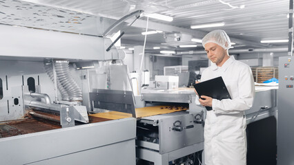 Chocolate factory man worker inspecting production line conveyor with sweets candy. Concept food industry banner