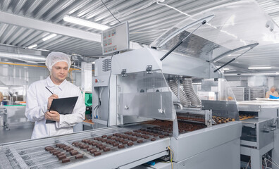 Chocolate factory man worker inspecting production line conveyor with sweets candy. Concept control food industry