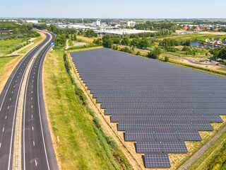 Aerial view of solar panels on gras in solar energy farm near highway.