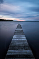 Obraz premium Pier into the Ocean at sunset with clouds.