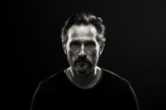 Monochrome portrait of mid aged lonely man. Black and white photo of male in black t-shirt on dark backdrop.