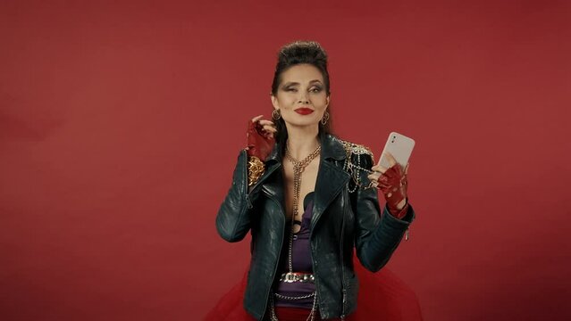 Informal woman takes a selfie, shoots a video on a smartphone in a studio on a red background. A woman poses, straightens her hair, blowing kiss to front camera with pout lips. Video 2 in 1.