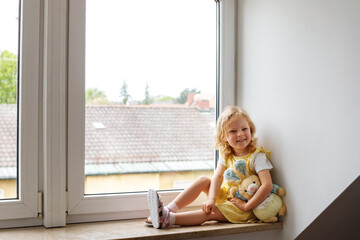 cute baby at home in a white room sits near the window. Beautiful toddler girl with teddy bear. A...