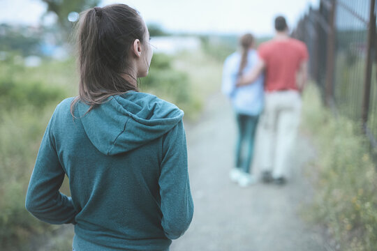 back view of romantic couple on the trail at the summer at sunset. A single lonely woman is walking behind and looking at a couple