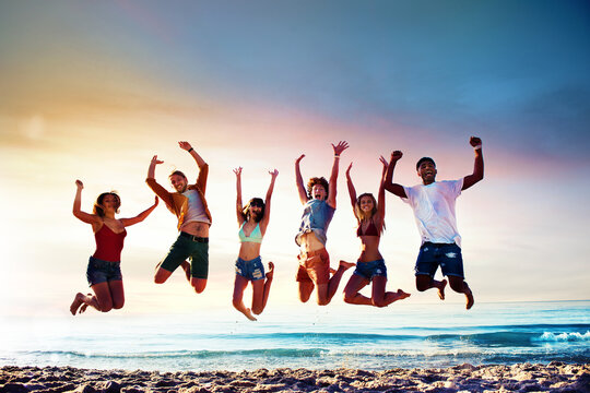 Happy smiling friends jumping over the sea of the beach