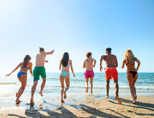 Group of friends run to the blue sea. Concept of summertime
