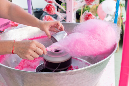 Woman making pink cotton candy at a street fair food stall.
