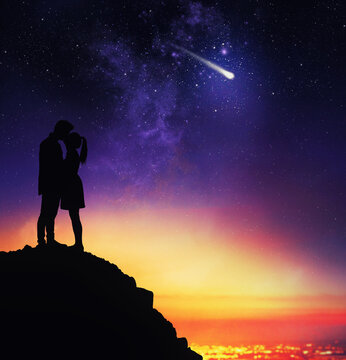 Couple of lovers in backlight from above a mountain expresses a desire during the sight of a falling star