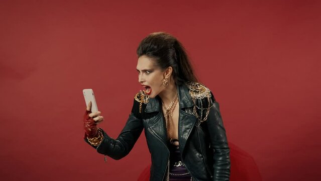 Freak woman aggressively talking on video call on smartphone on a red background. The woman presses the phone, interrupting the conversation and screams loudly, dropping her irritation.