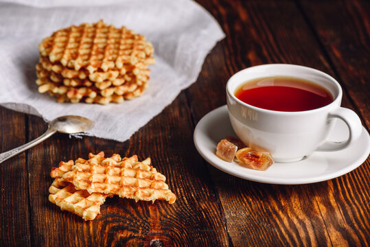White Cup of Tea with Waffles Stack on Napkin and Pieces of Waffle on Wooden Surface.