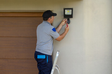 Image of an electrician on a scissor ladder using his tools to install a spotlight on a house....