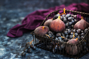 Fresh figs and purple grape in basket on dark wooden background