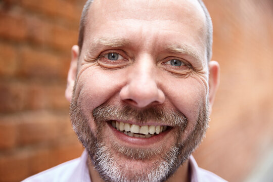 Close-up headshot portrait of real mature smiling man against a brick wall.
