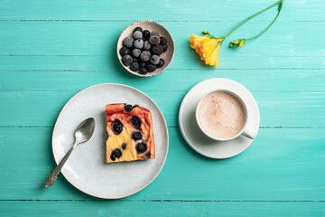 A cup of coffee and blueberry cake, frozen blueberries and yellow freesia flower on turquoise wooden table. Top view, flat lay