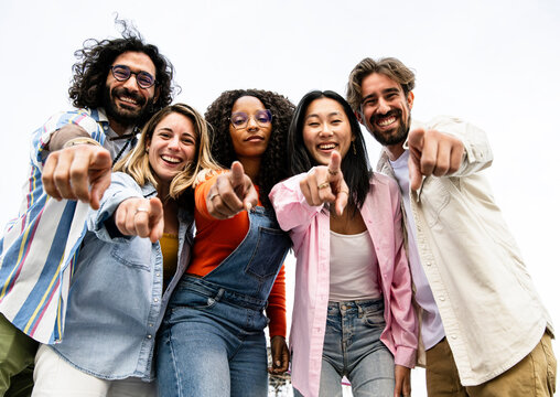 Low view of cheerful multiracial group of young hipsters pointing and looking at camera. Happy diverse group of young hipsters staring at camera outside and pointing fingers at the camera.