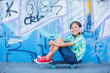 Cute boy with skateboard outdoors, standing on the street with different colorful graffiti on the walls, hipster style, cool fashion