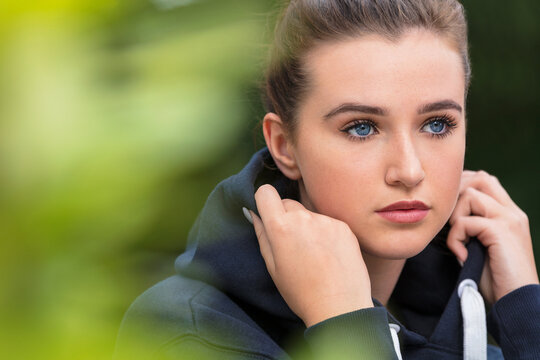 Beautiful girl teenager female young woman with blue eyes outside wearing dark blue hoody looking sad depressed or thoughtful