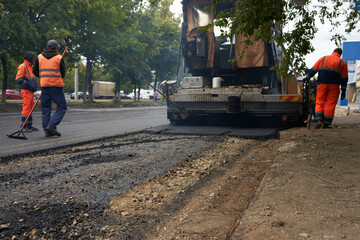 Repair of the road.  Asphalt paver puts asphalt mortar on the road. Nearby are road workers.