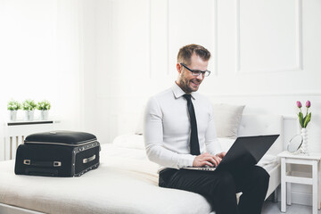 Young businessman on bed working with a laptop from his hotel room