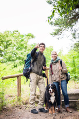 Naklejka na ściany i meble Young hiker couple with Bernese mountain dog on forest trail