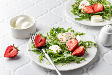 Salad with mozzarella with strawberries, mozzarella and arugula. Healthy light summer salad modern styling on white tile background
