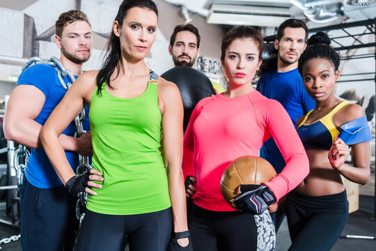 Group of women and men in gym posing at fitness training standing together with gear and dumbbells